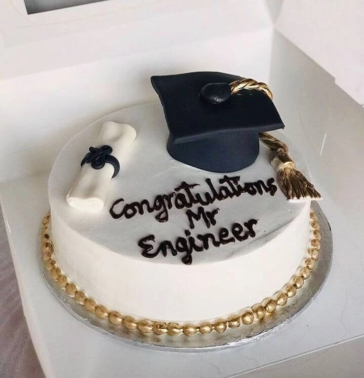 White graduation cake with a black cap a golden tassel. a diploma decoration. and the message 